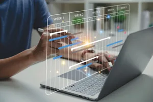 person using a laptop with a digital project management timeline overlay, showing tasks and weeks, in a modern workspace.